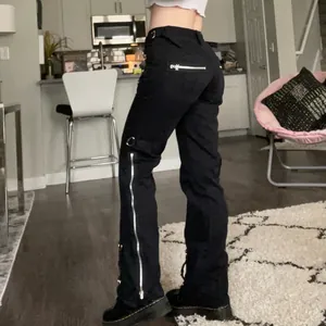 Gedetailleerde weergave van zwarte flare broek met lage taille, ritsen en metalen ringen