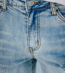 Gros plan détaillé sur un short en jean délavé bleu clair avec bouton en métal et coutures.