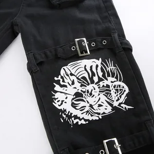 Close-up van zwarte streetwear jeans met metalen gespen en een witte grafische print.