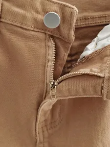 Gros plan sur le détail de la fermeture éclair et du bouton du jean tan