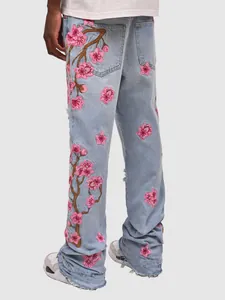 Detail showing pink cherry blossom embroidery on men's light blue streetwear jeans.