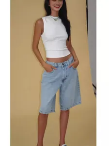 Detail shot of a woman in light blue denim bermuda shorts and a white sleeveless top.