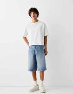 Full body view of men's loose light blue denim shorts styled with white t-shirt