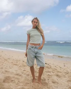 Western style light wash denim bermuda shorts worn by a model in a beach setting