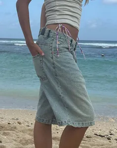 Detail view showing the slim fit and side drawstring of denim shorts on a sunny beach