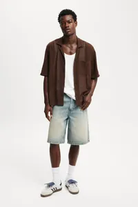 Full body shot of men's light wash loose fit denim shorts styled with a brown knit shirt