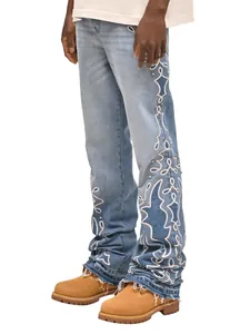 Dettaglio di jeans azzurri da uomo con ricami laterali bianchi e orlo a frange.
