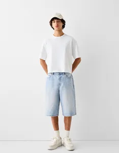 Full body view of stylish men's loose fit light blue wash denim shorts with a white t-shirt