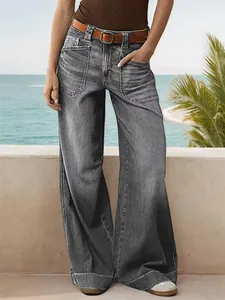 Detail of grey wide-leg denim jeans with a brown belt against a coastal backdrop