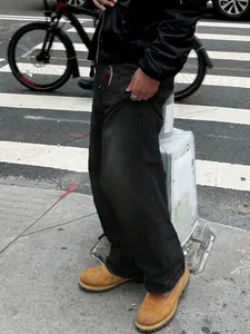 Vista laterale di jeans neri larghi da uomo abbinati a stivali color cuoio per strada