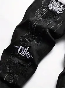 Detailed view of heavy skull embroidery and distressed texture on black denim jeans