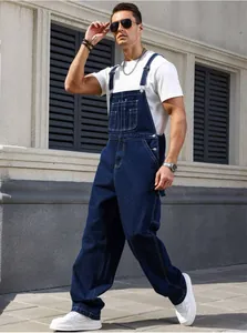 Full body view of man wearing retro loose straight-leg denim overalls in navy blue