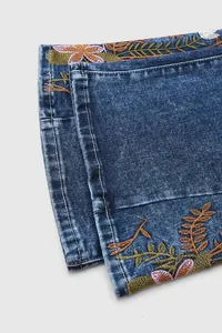 Close-up macro view of delicate floral embroidery at the hem of blue flared denim jeans for women
