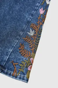 Close-up of intricate floral embroidery details on the hem of blue denim flare jeans.