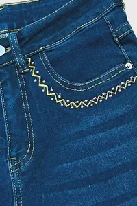 Detailed view of yellow zigzag and pink floral embroidery on blue denim jeans pocket
