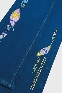 Detailed view of colorful feather and geometric embroidery on dark blue denim pants