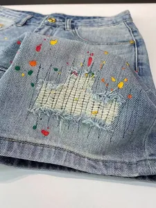 Close-up detail of distressed denim shorts featuring colorful paint splatters and frayed edges