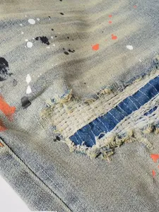 Detailed close-up view of vintage distressed denim jeans with paint splatters and patches
