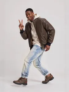 Modello in posa con jeans dritti lavati in blu neve e una giacca di pelle marrone