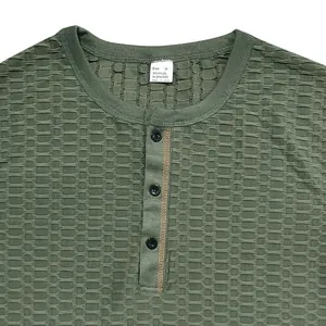 Close-up van olijfgroen Henley T-shirt met textuur, contraststiksels en zwarte knopen.