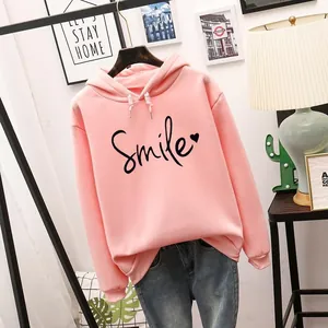 Vista detallada de sudadera rosa con capucha y estampado Smile en ambiente de hogar