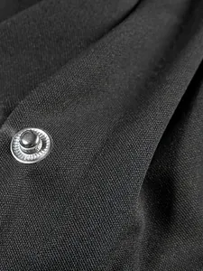 Macro close-up of high-quality black textured fabric and silver snap button on baseball jacket