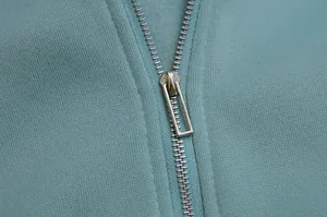 Detail of a silver metal half-zipper on a light blue fleece-lined cropped hoodie.