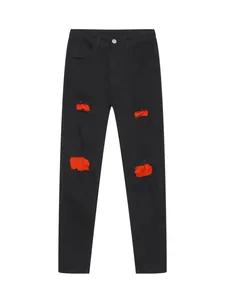 Detailed view of slim fit black jeans featuring vibrant red distressed patch accents