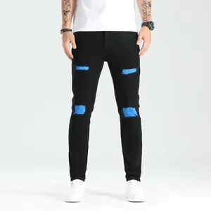 Dettaglio ravvicinato di jeans skinny neri da uomo con vivaci e moderne toppe blu.