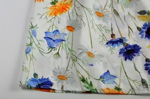 Detailansicht der Blumenmuster und Saumnähte eines weißen Herbstkleides für Damen