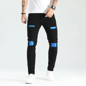 Dettaglio dei jeans neri strappati da uomo con toppe blu vivaci sulle ginocchia.