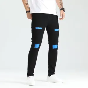 Dettaglio jeans skinny neri da uomo con strappi e toppe blu, stile trendy e tessuto elastico.