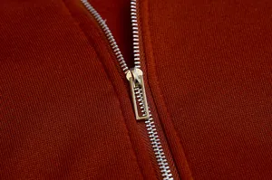 Macro shot of a high-quality silver metal zipper on a rust orange knitted fleece hoodie