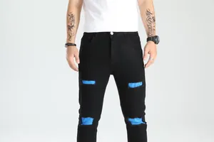 Dettaglio dei jeans neri strappati da uomo con toppe in tessuto blu brillante