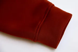 Close-up of ribbed cuff and fleece fabric on a terracotta red hooded sweatshirt