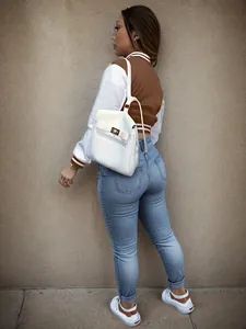 Stylish brown and white varsity jacket for women styled with jeans and a backpack.