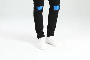 Vista dettagliata di jeans skinny neri strappati da uomo con patchwork blu e sneakers bianche