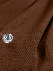 Macro detail of a silver snap button on brown woven fabric of a women's baseball jacket