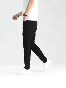Jeans neri strappati slim fit elasticizzati da uomo con dettagli patch, posa di profilo