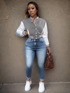 Detailed view of a trendy grey and white color-block varsity jacket worn with denim jeans