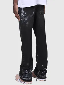 Detailed view of men's black straight-leg jeans with white paint splatter and frayed hems