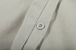 Close-up detail of light grey linen fabric texture and button on a casual shirt.