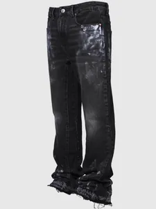 Detail of men's black straight leg jeans with paint splatter and raw hem edges.