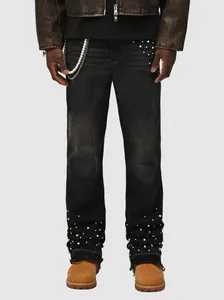 Detail of men's black stacked jeans with pearl embellishments and metal chain accessory