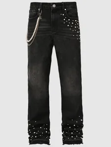 Detailed view of men's black straight-leg jeans with pearl embellishments and stacked hem.