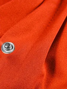 Macro detail of orange varsity jacket fabric with silver metal snap button closure