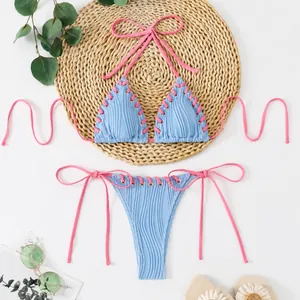 Detail view of light blue textured bikini featuring pink contrast lacing and halter ties.