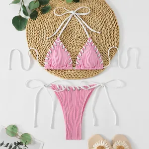 Detail view of a pink ribbed bikini set with white lacing on a straw mat background.