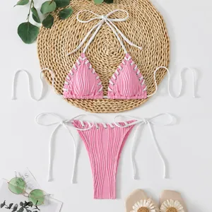 Detail view of a pink ribbed bikini set with white lacing on a straw mat background.