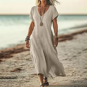 Detail view of a loose V-neck linen maxi dress on a beach, showcasing airy boho style.